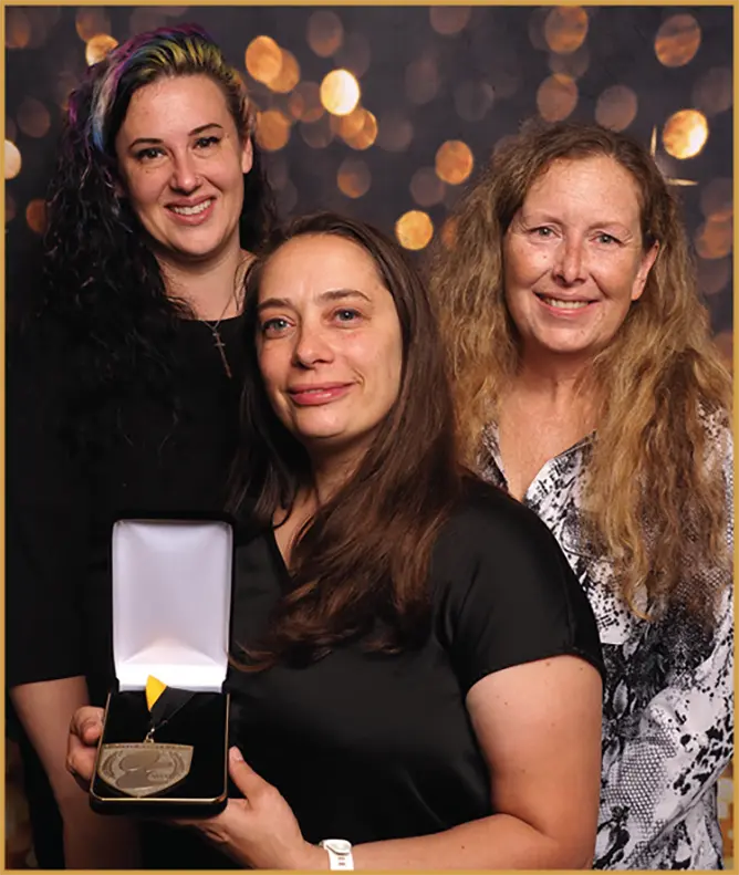 Three women from Pro Groomer Network hold up an award together as they smile