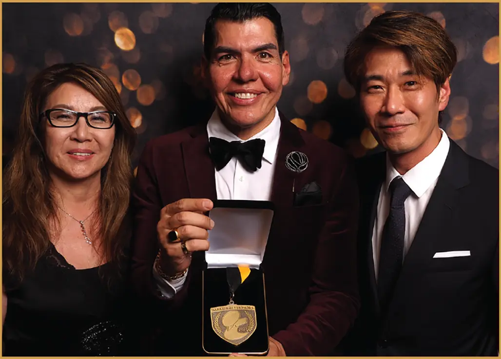 Victor Rosado holds up an award alongside another woman and man as they all smile together