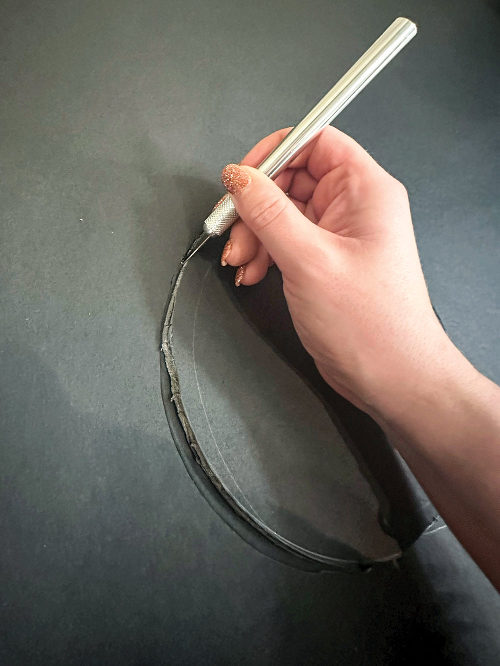 Close-up portrait photograph perspective of a person using an X-Acto Knife to cut out a circle shape on the Black Tri-fold Foam Presentation Board