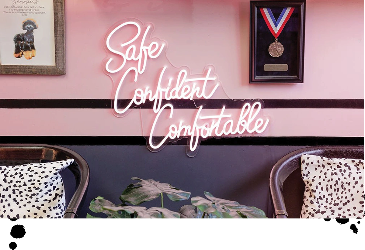 Pink wall with a neon sign saying "Safe, Confident, Comfortable" and a black and white themed decor.