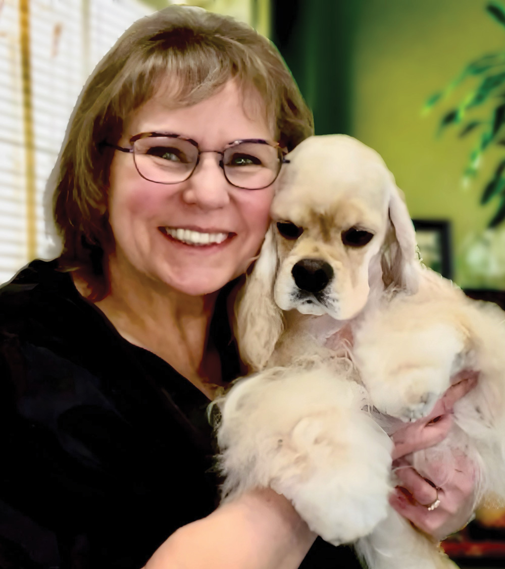 Person smiling and holding a fluffy, cream-colored dog indoors.