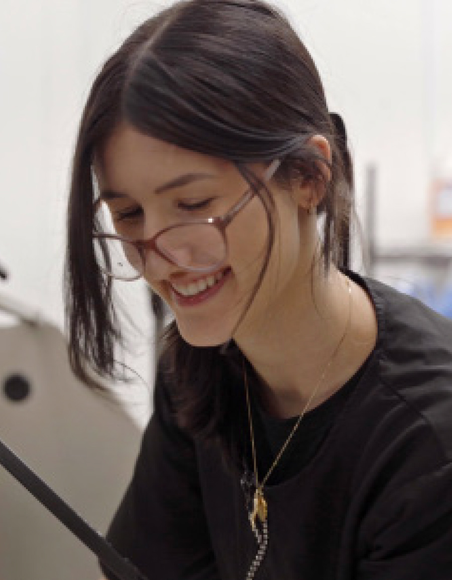 smiling woman with dark hair tied back, wearing glasses and a black grooming shirt