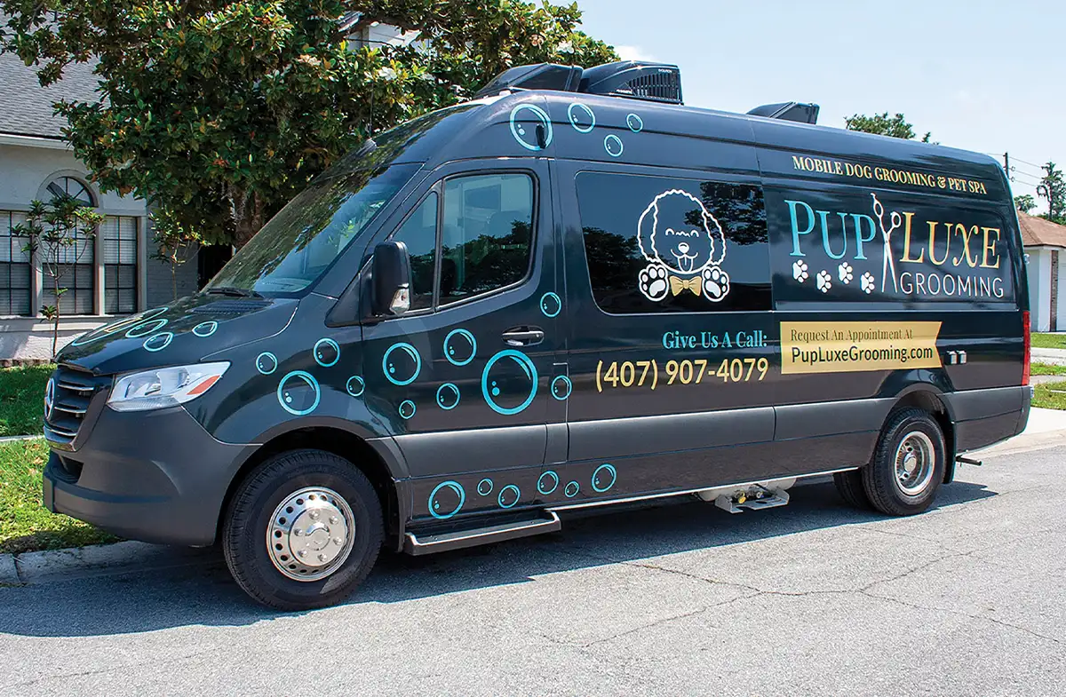 A black mobile dog grooming van with the "Pup Luxe Grooming & Pet Spa" logo and teal bubbles, parked on a residential street.