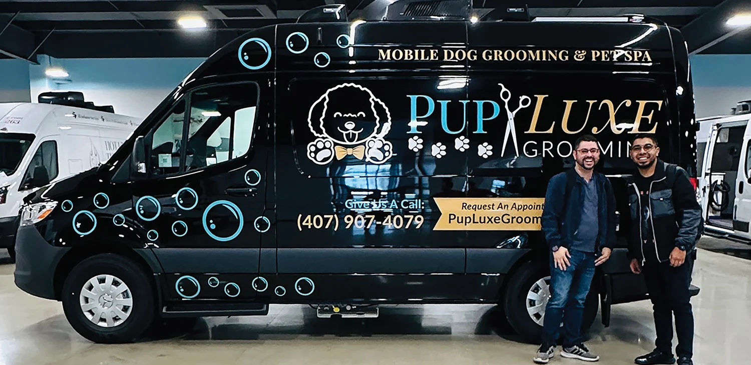 A black mobile dog grooming van with the "Pup Luxe Grooming & Pet Spa" logo and two men standing next to it.