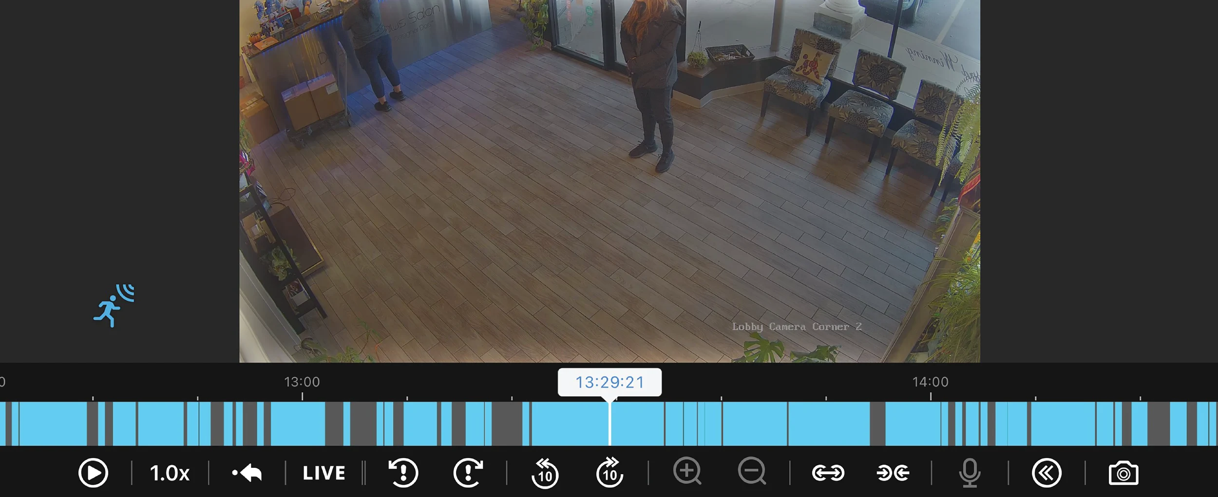 Digital interface for a lobby security camera showing two people in a salon. A blue timeline at the bottom indicates recorded motion events with various playback icons.