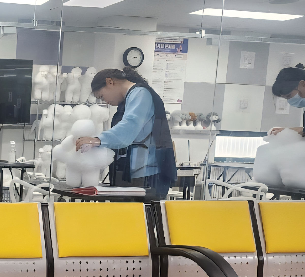 A pet groomer practicing on a white, fluffy poodle-shaped model dog at a workstation