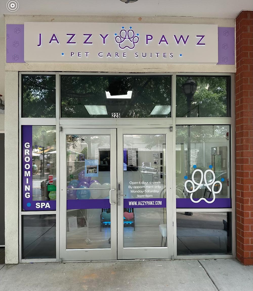 The glass storefront entrance of Jazzy Pawz Pet Care Suites with a purple and white sign above the doors.