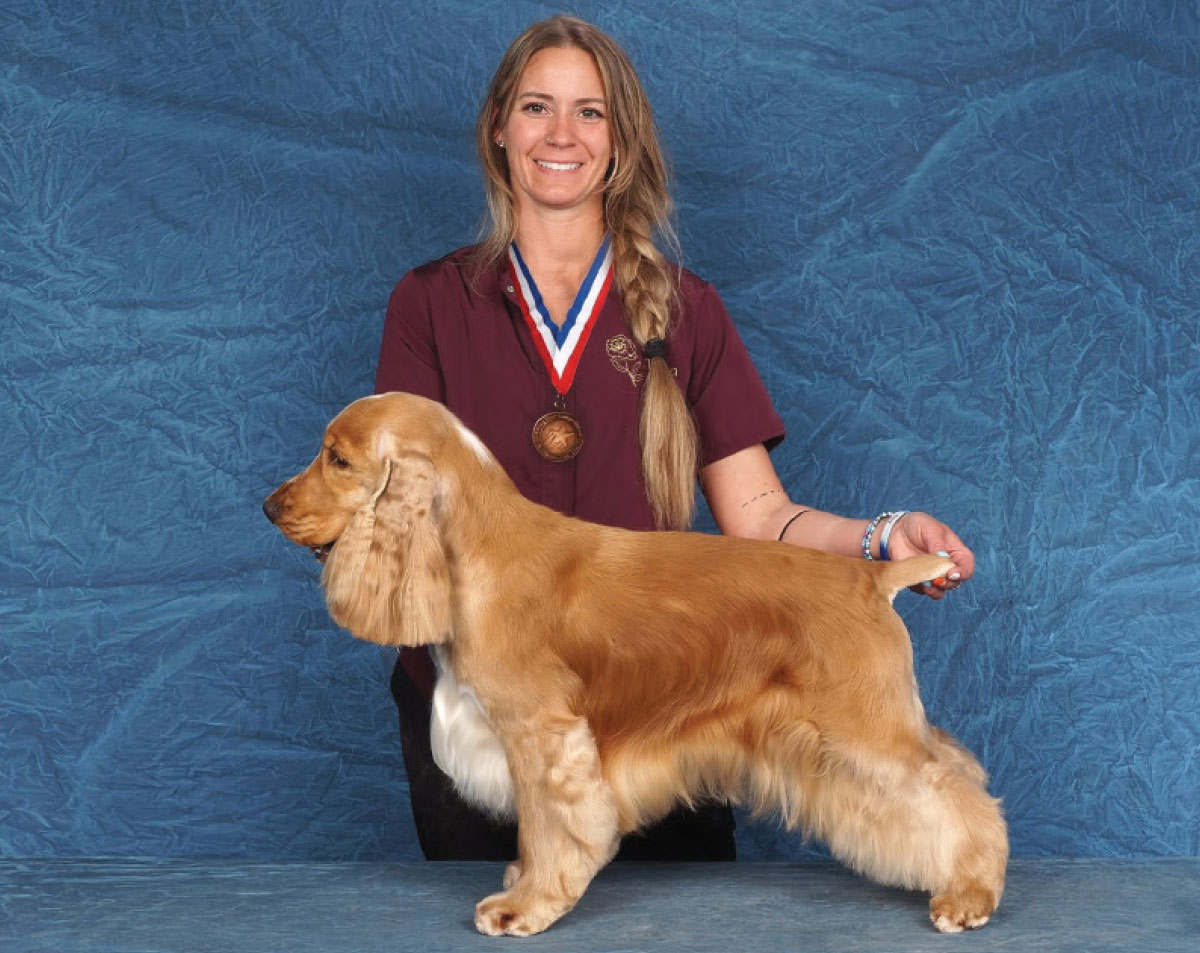 Woman wearing a medal poses a golden English Cocker Spaniel against a blue backdrop.