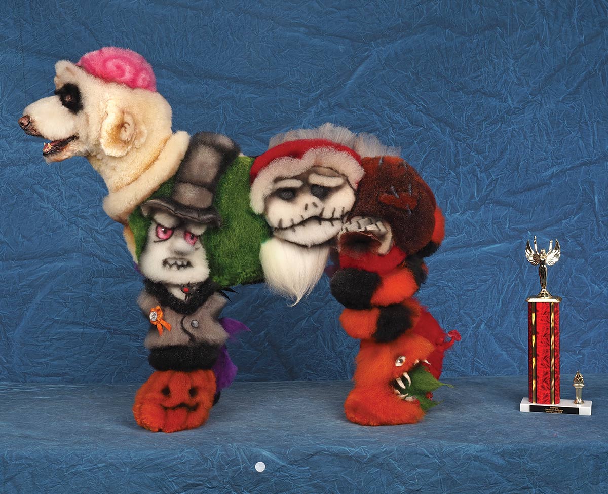 Side view of a Poodle creatively groomed and dyed with elaborate Halloween characters, including Jack Skellington, next to a trophy.