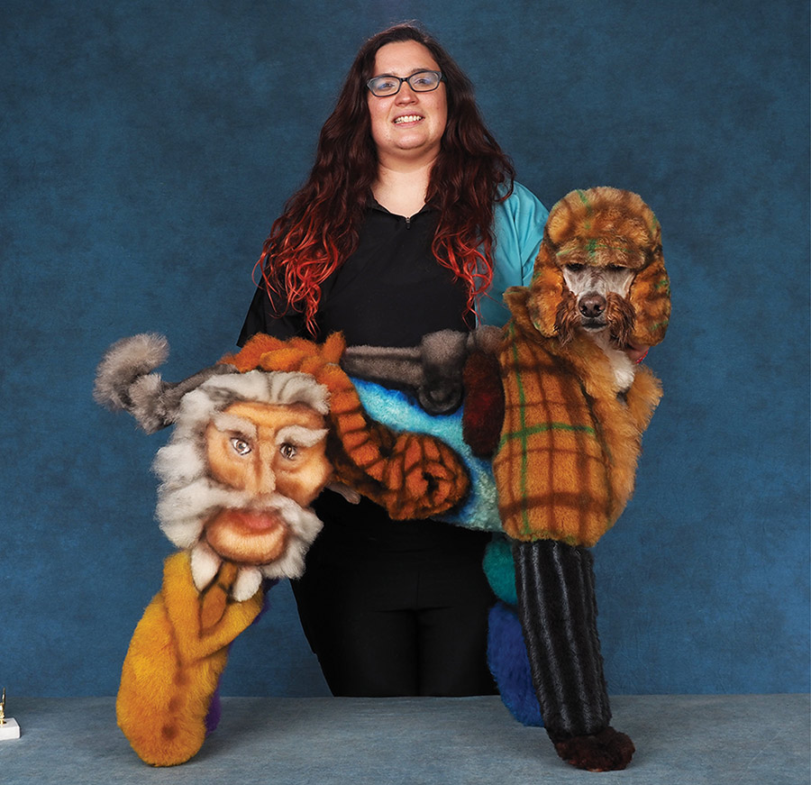 A groomer displays the other side of a Standard Poodle creatively styled with Clue characters and patterns.
