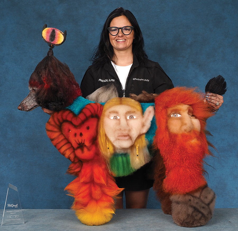 A groomer holding an award stands behind a Standard Poodle creatively groomed with Lord of the Rings character designs.