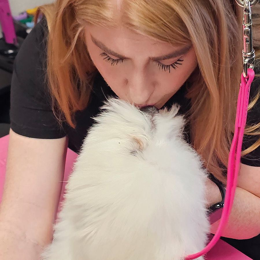A woman leaning down to kiss a fluffy white puppy's forehead on a table.