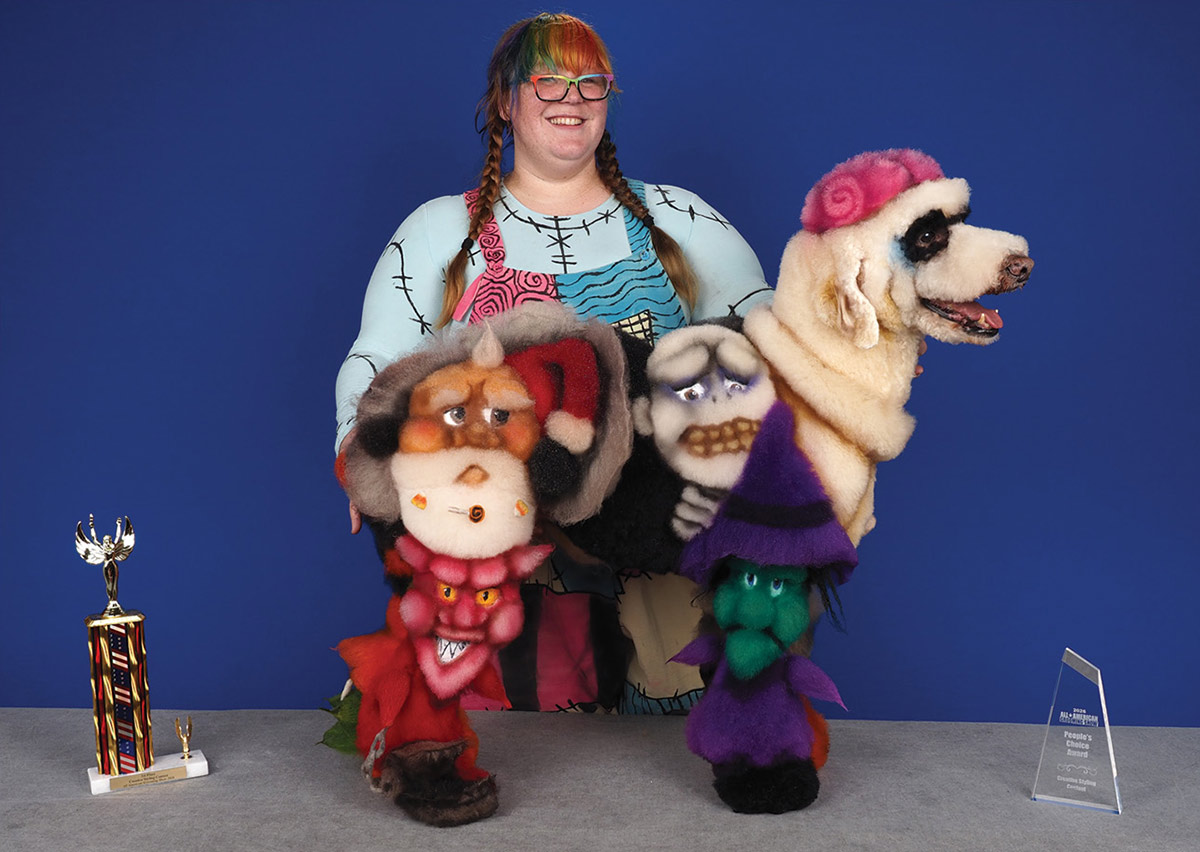 A groomer dressed as Sally stands behind a poodle creatively dyed with Nightmare Before Christmas characters, posing on a table next to a trophy and People's Choice award plaque.